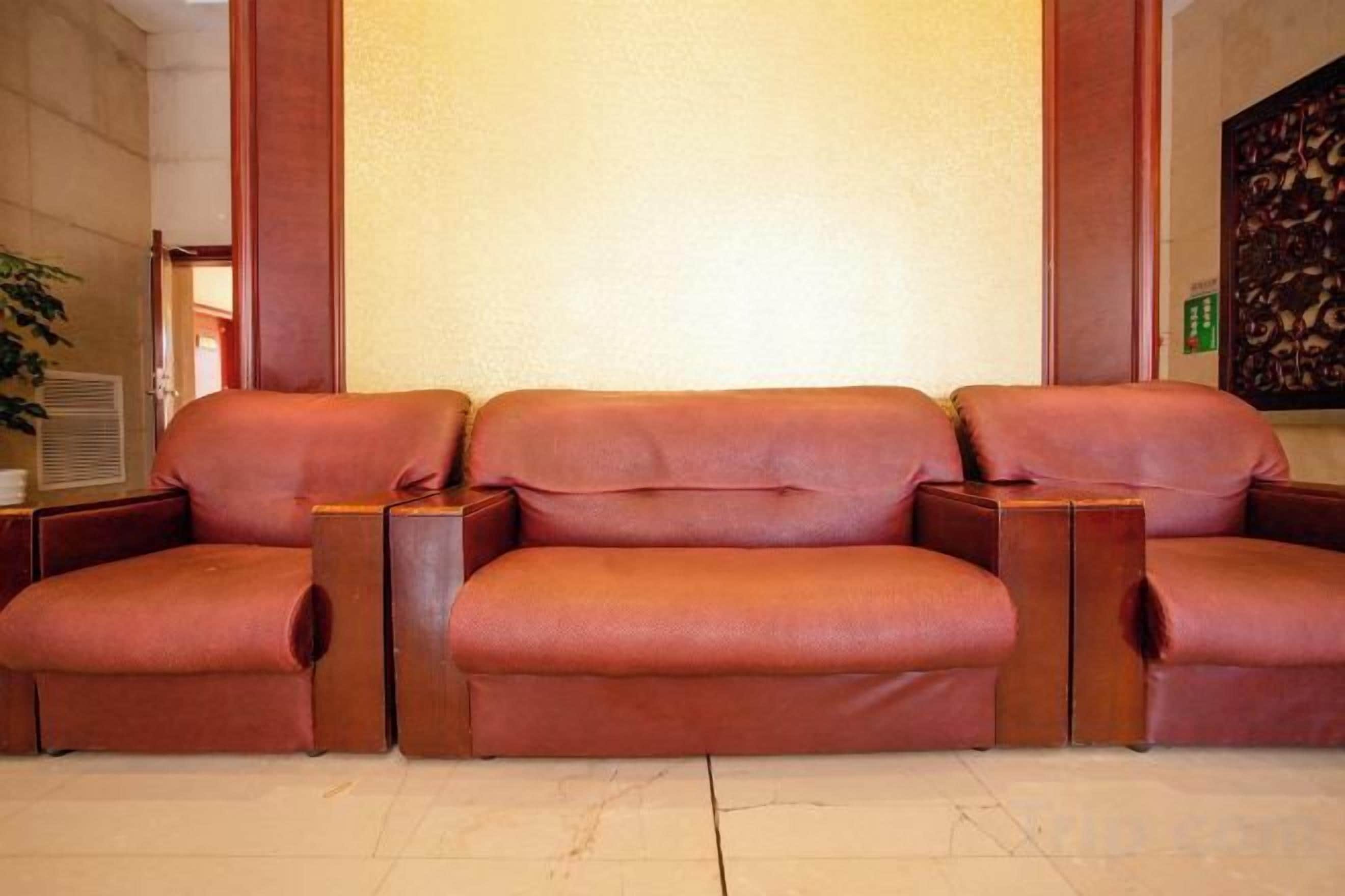 A three-seater sofa with armrests, positioned against a wall with a large, plain background.