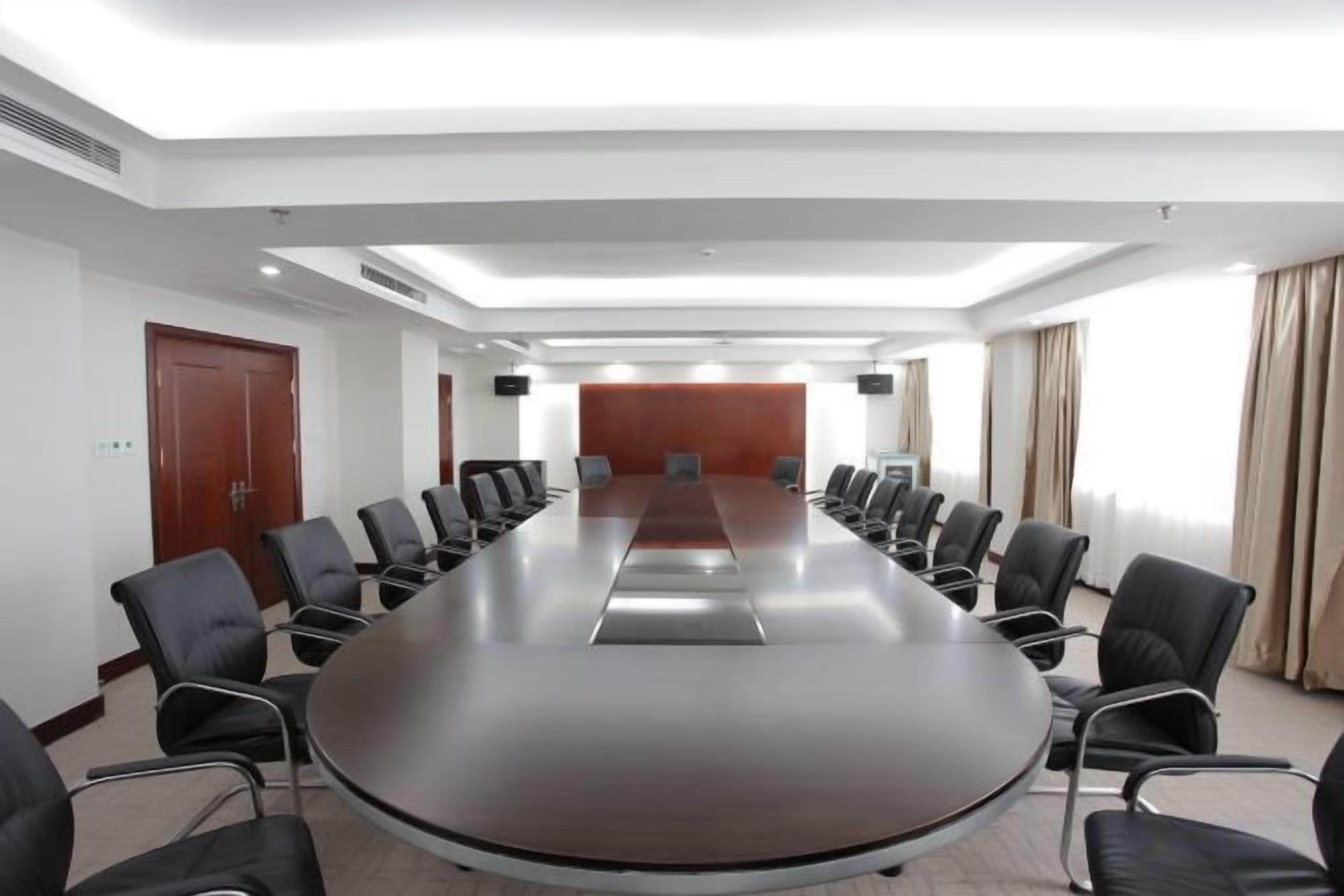 A conference room with a long table and chairs, white walls, and a wooden door.