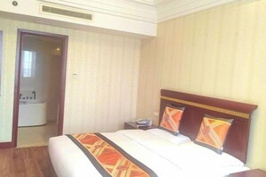 Habitación de hotel con cama, mesita de noche, teléfono y baño visible a través de una puerta abierta.