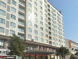Un hotel de varios pisos con fachada moderna, un acceso cubierto y un cielo despejado.