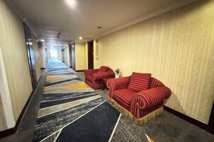 A hotel corridor with a carpeted floor, two red-striped sofas, and a patterned wall.