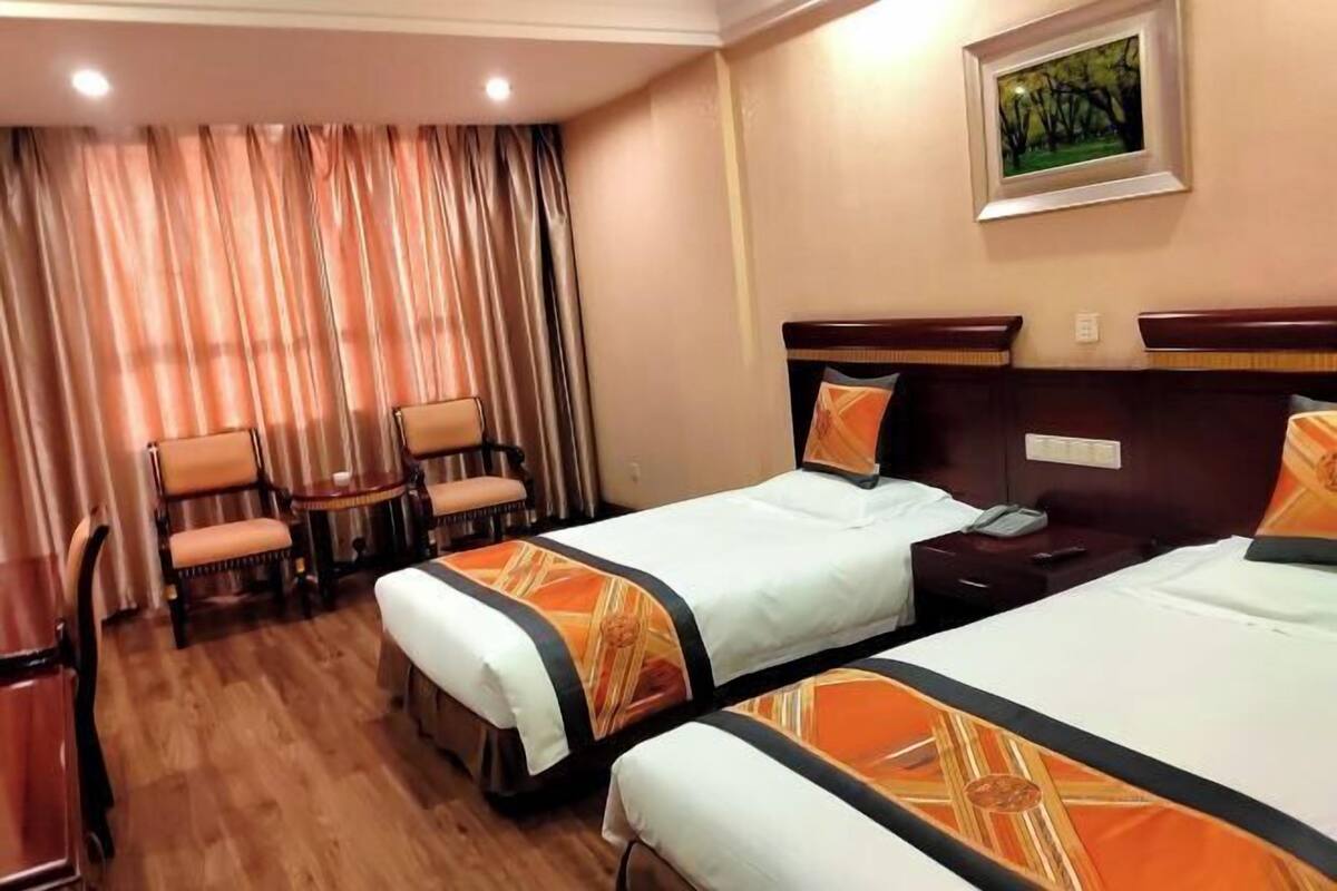 A hotel room with two beds, a desk, a chair, and a painting on the wall.