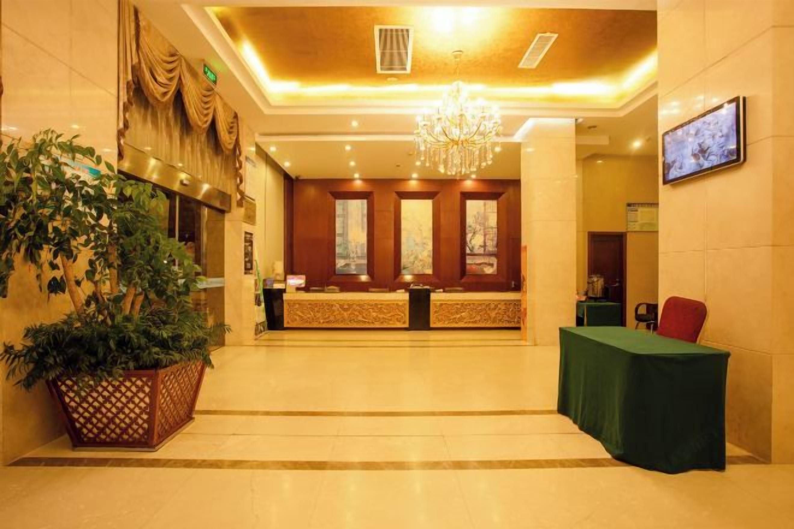 A hotel lobby with a reception desk, a chandelier, and a large potted plant.