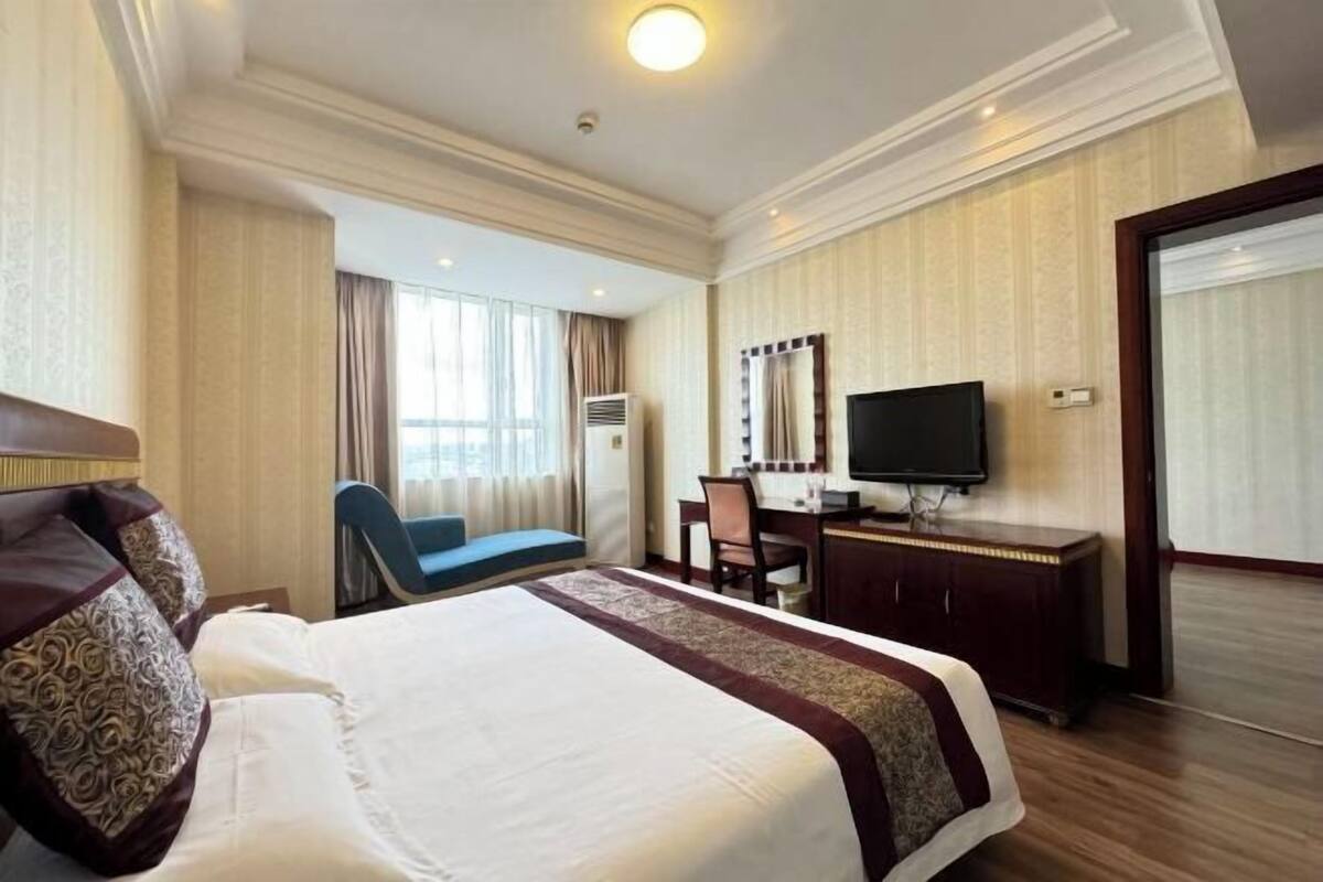 A hotel room with a large bed, a desk, a chair, a television, and a window with curtains.