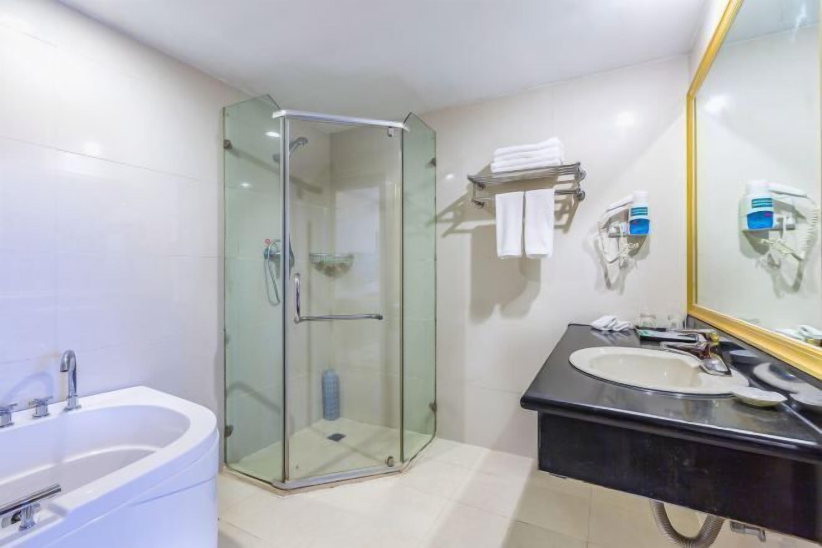 A bathroom with a glass-enclosed shower, a white bathtub, a black sink, and a mirror with a gold frame.
