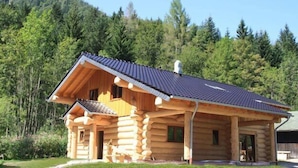 Una baita di legno con tetto spiovente e balcone, immersa in una fitta foresta.