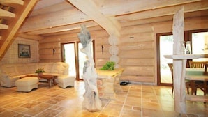 Interno di una baita di legno con pavimento in pietra, una scala, un divano bianco, un tavolo da pranzo e una scultura decorativa in pietra.
