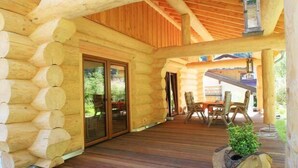 Una baita di legno con veranda, porta scorrevole in vetro e zona pranzo con mobili da esterno.
