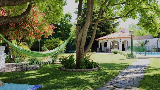 A garden with a hammock, a pool, and a building with arches. - Chiara Lodge (Chacras de Coria)