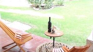 A patio with two wooden chairs, a small round table with a bottle and glass, and a hanging plant. - Chiara Lodge (Chacras de Coria)