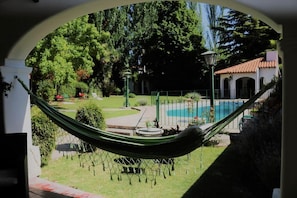 A hammock in a garden with a pool and a building in the background.