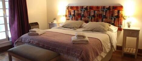 A neatly made bed with a headboard, a bedside table with a lamp, and a window with curtains.
