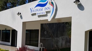 The exterior of the Yolonam Inn Hotel with a clear entrance, a white facade, and a logo featuring a stylized bird and wave design. - Yolonam Inn (Tuxtla Chico)