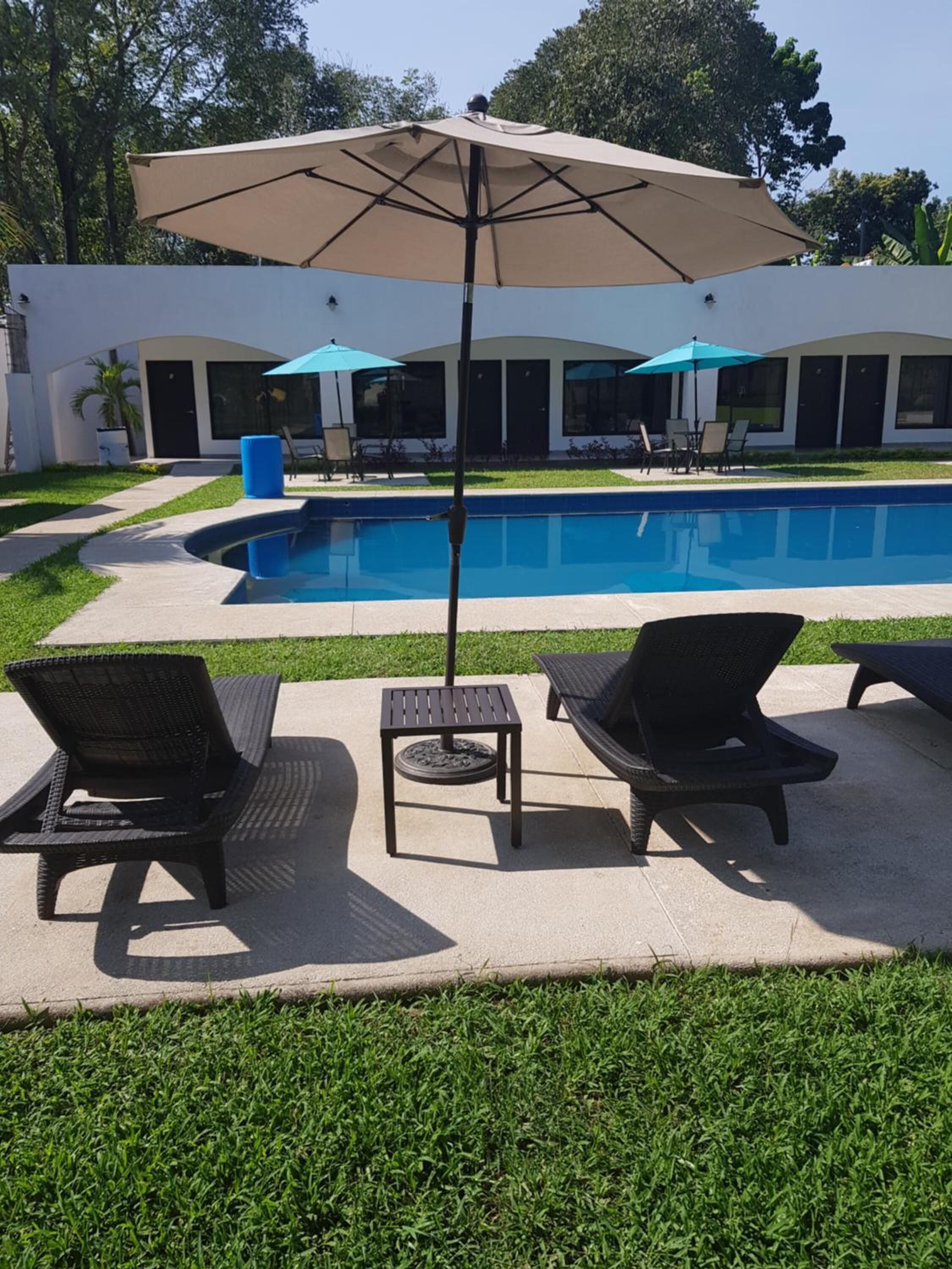 Un área junto a la piscina con dos sillas de descanso, una mesa y una sombrilla grande.