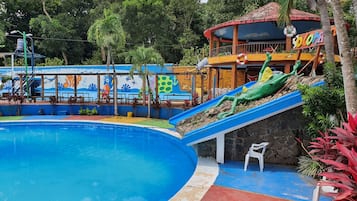 A swimming pool with a slide, surrounded by a mural, and a building with a sign.
