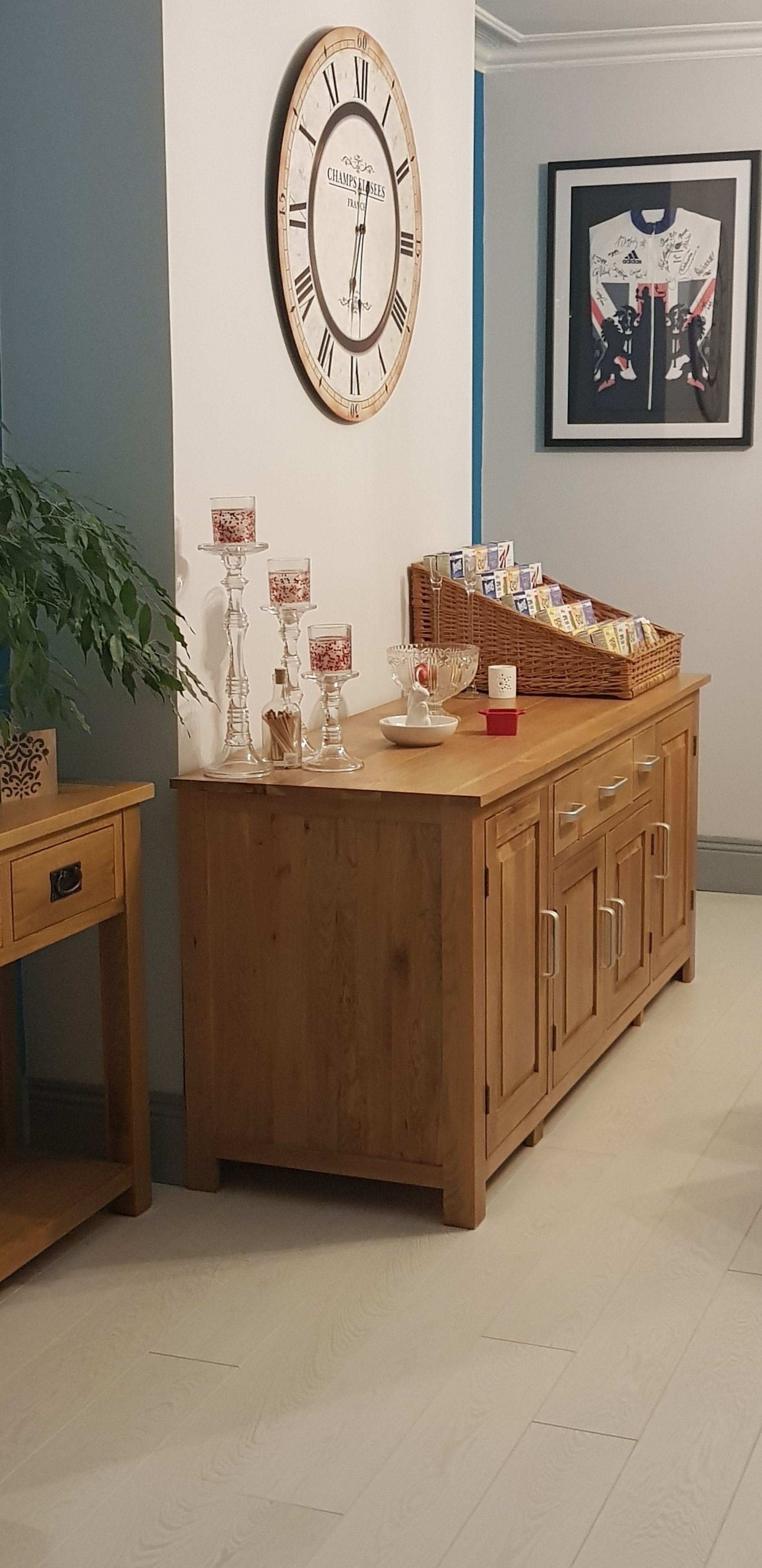 A wooden cabinet with glass candle holders, a framed clock, and a framed poster on the wall.