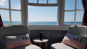 Two patterned armchairs facing a bay with a view of the sea and a distant ship. - Brunswick Bed & Breakfast (Weymouth)