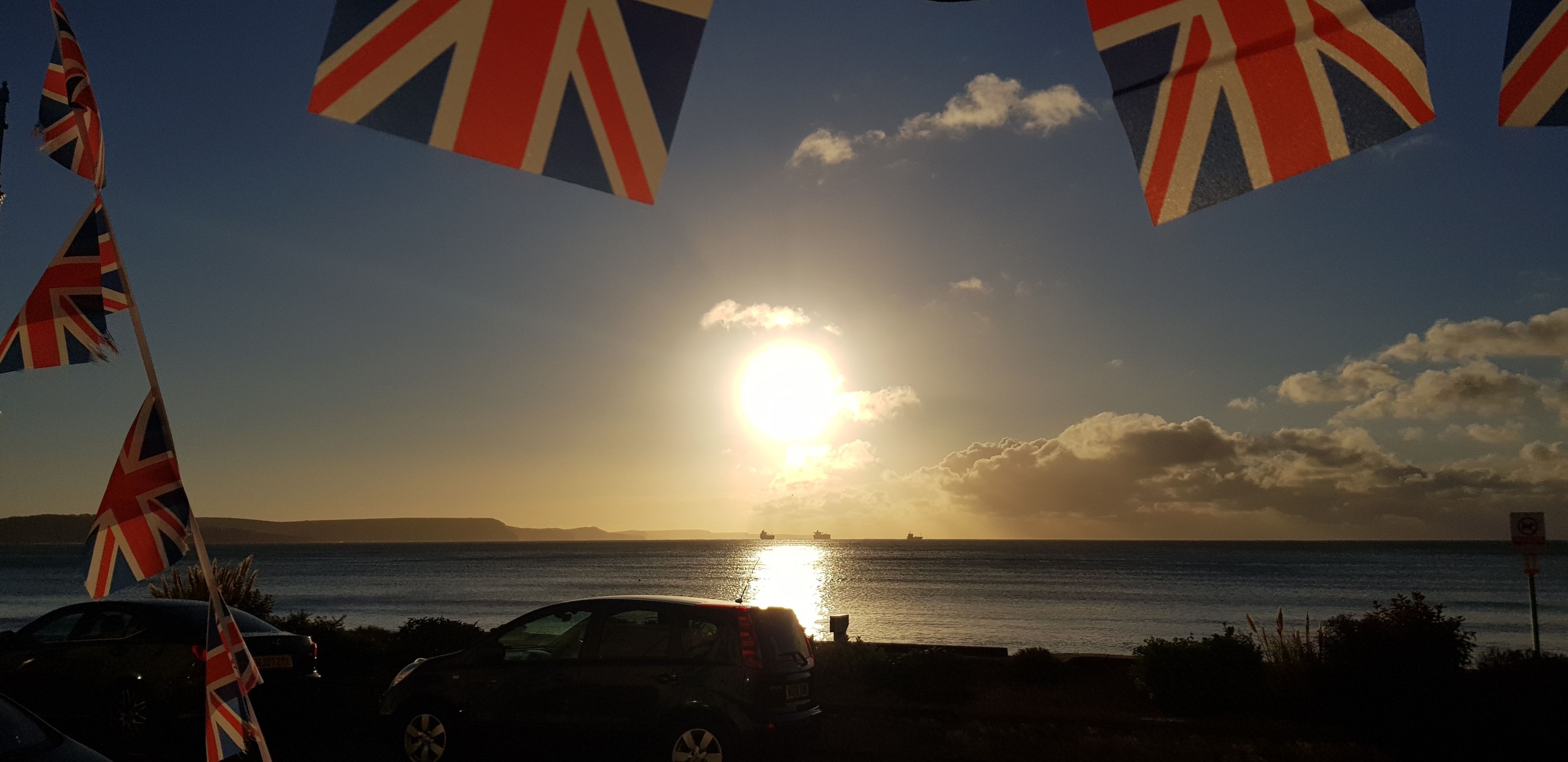 A sunset over a body of water with flags and a car in the foreground.
