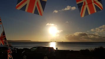 A sunset over a body of water with flags and a car in the foreground.