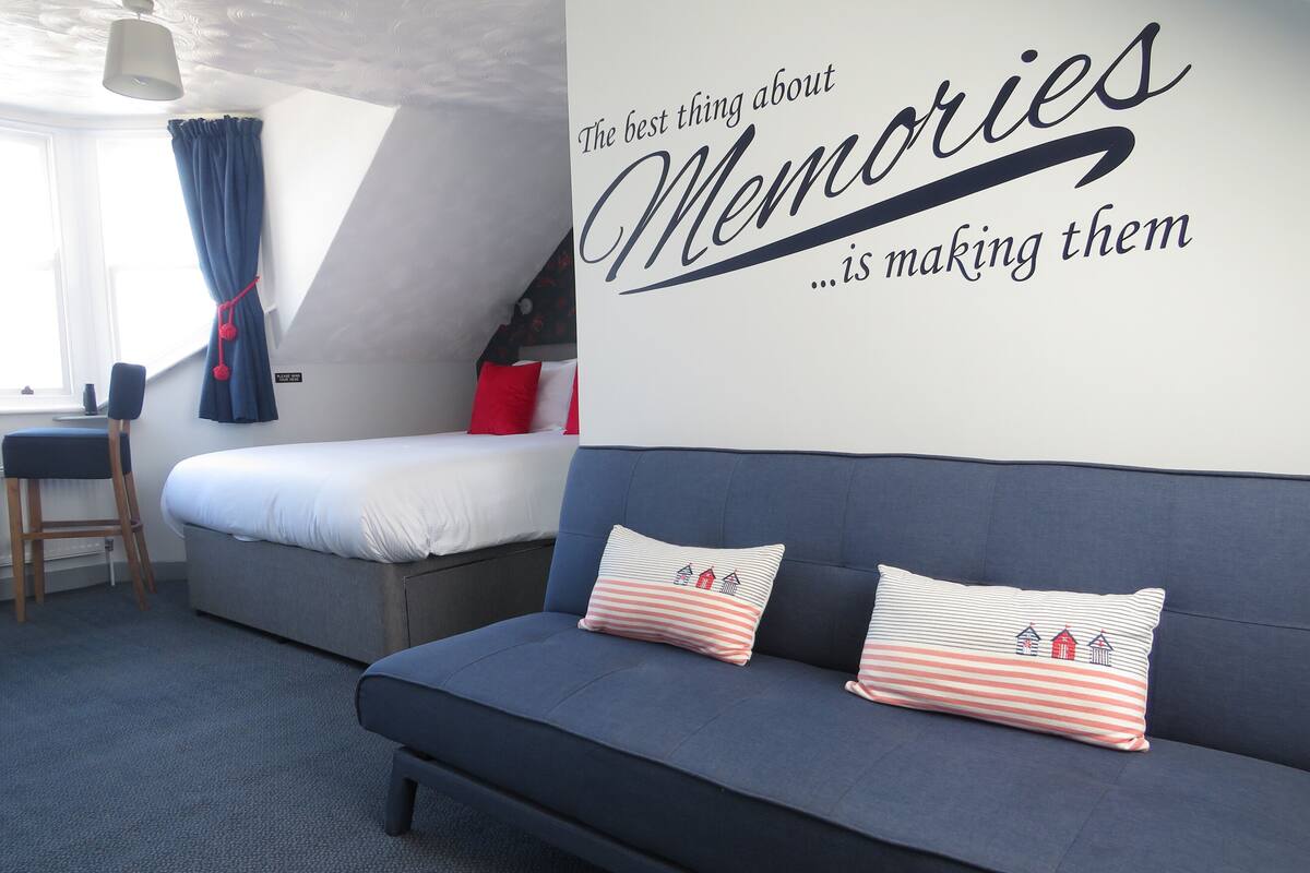 A bedroom with a bed, a sofa, and a wall with a quote about memories.