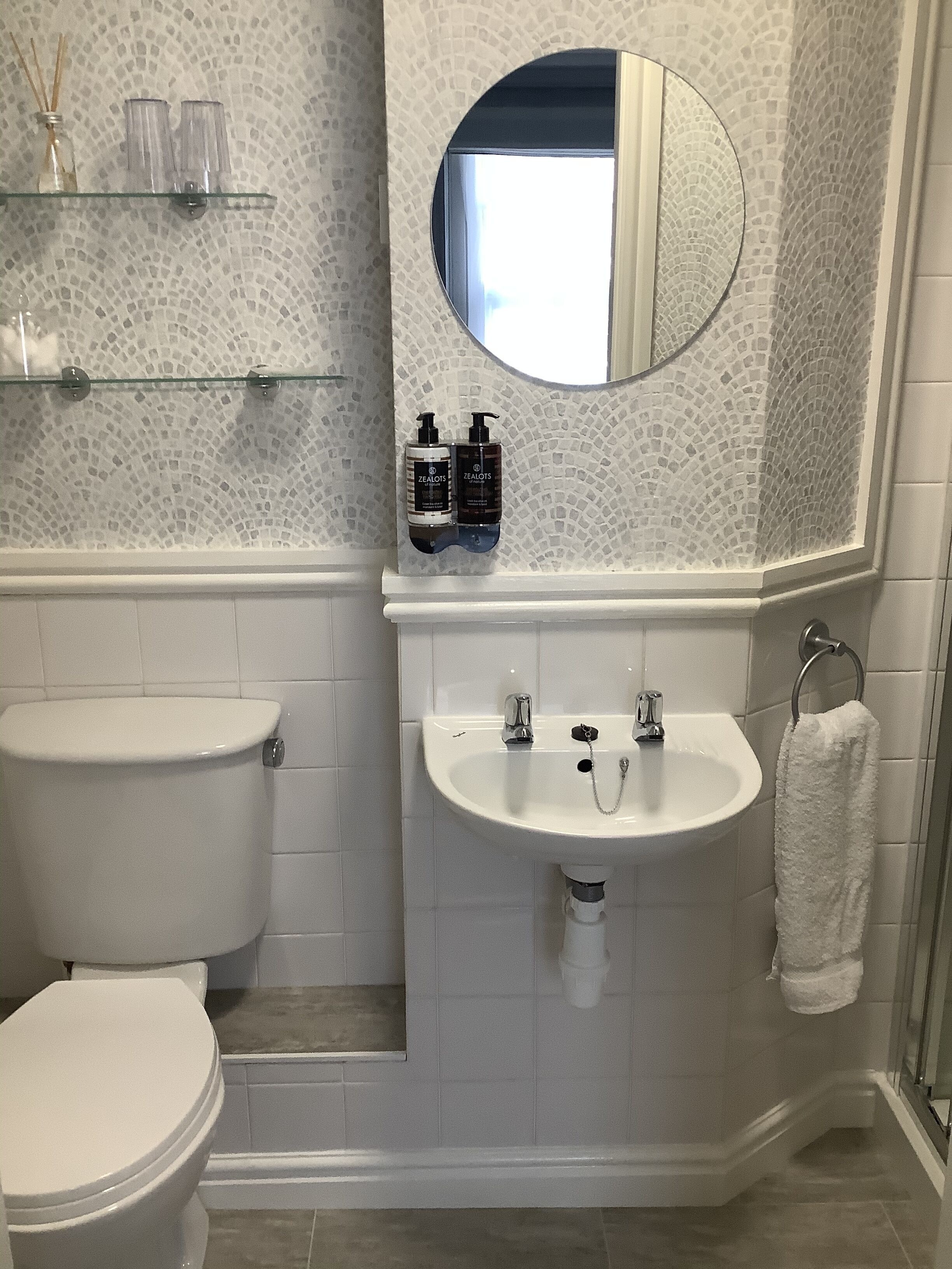 A bathroom with a toilet, sink, and mirror. There are two bottles on the shelf above the sink.