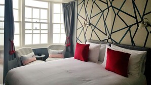 A hotel room with a large bed, two chairs, a small table, and a geometric-patterned wall. - Brunswick Bed & Breakfast (Weymouth)