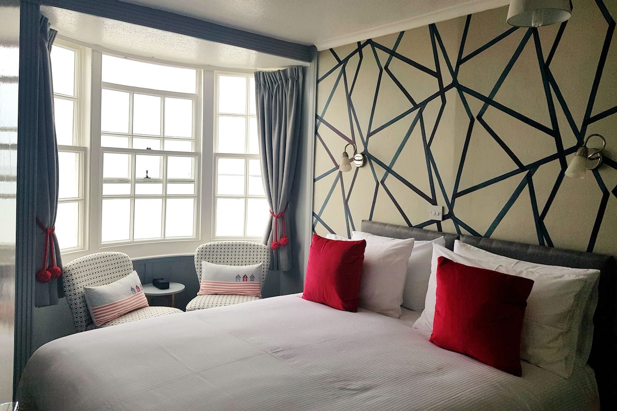 A hotel room with a large bed, two chairs, a small table, and a geometric-patterned wall.