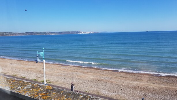 A coastal view with a pebbly beach, a person walking, and a clear sky. - Brunswick Bed & Breakfast (Weymouth)