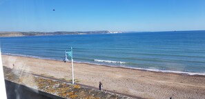 A coastal view with a pebbly beach, a person walking, and a clear sky. - Brunswick Bed & Breakfast (Weymouth)