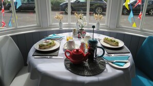 A dining area with a table set for breakfast, including plates of food, a coffee pot, and a view of parked cars outside. - Brunswick Bed & Breakfast (Weymouth)