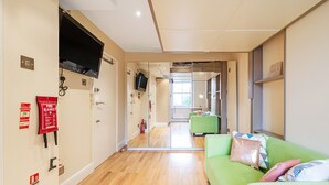 A hallway with a green sofa, a fire blanket, and a television mounted on the wall. - London Villa - 43 Clanricarde Gardens (London)