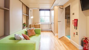 A compact room with a green sofa, a small table, a window, and a door leading to a bathroom. - London Villa - 43 Clanricarde Gardens (London)