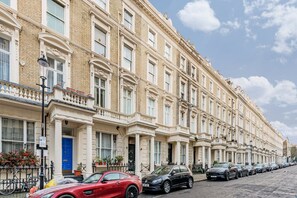 A row of traditional terraced houses with uniform architecture, a clear sky, and parked cars along the street.