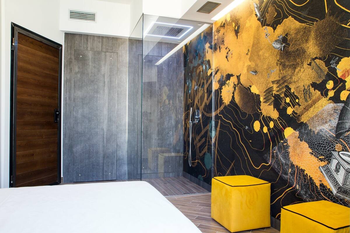 Une chambre moderne dotée d’un grand lit, d’une porte-cloison en verre et d’un mur orné d’une fresque à motifs.