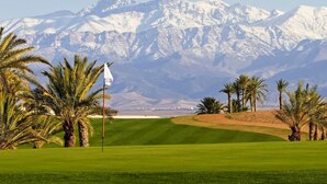 A golf course with a flagstick, palm trees, and snow-capped mountains in the background. - Villa Jasmine V4 70 Marrakesh (Marrakech)