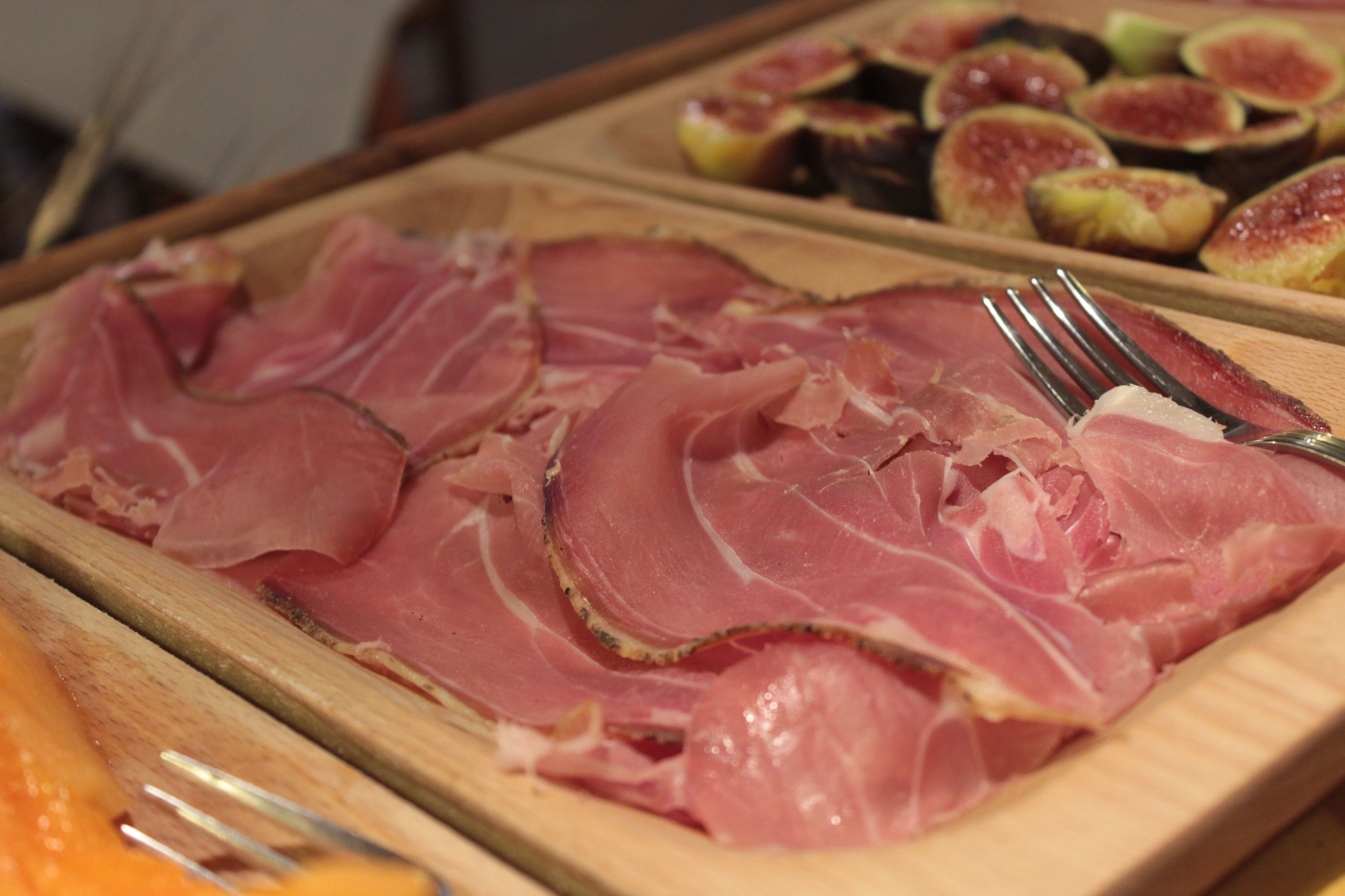 A wooden cutting board with sliced ham and figs.