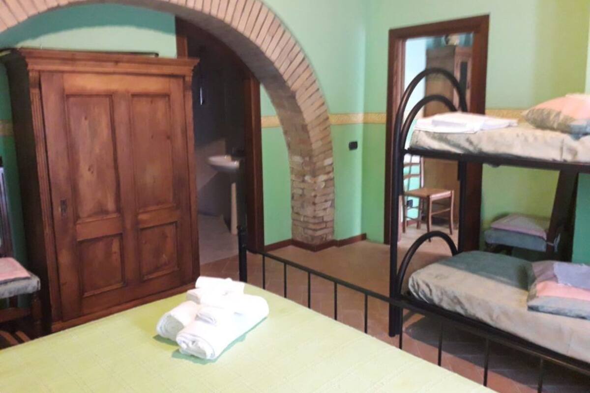 Une pièce avec un lit superposé, une armoire en bois et une arche en briques.
