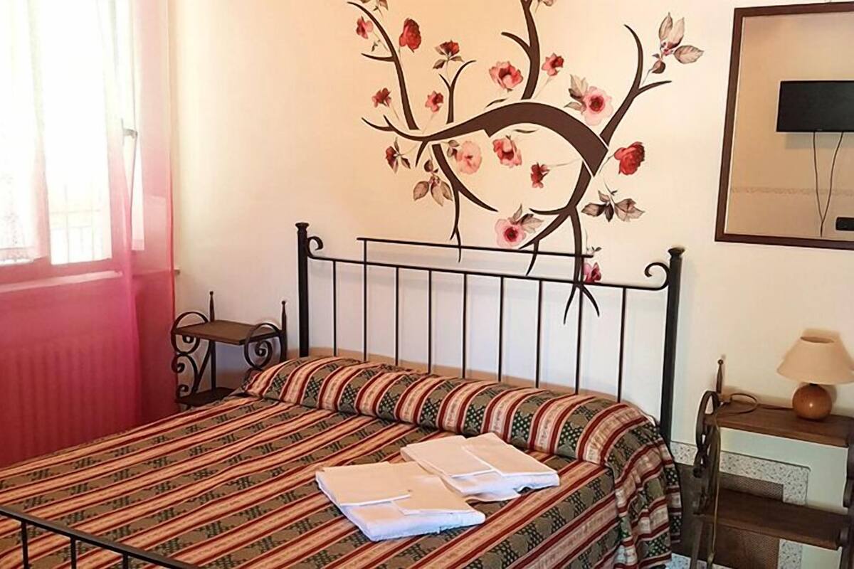 Un lit bien fait, avec une literie à rayures, un téléviseur fixé au mur et une petite table de chevet avec une lampe.