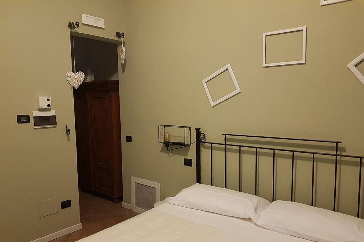 Une chambre d’hôtel avec un lit, un radiateur, une étagère fixée au mur et une porte donnant sur une autre pièce.