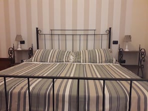 Una cama con colcha a rayas y estructura metálica, flanqueada por dos mesitas de noche con lámparas.