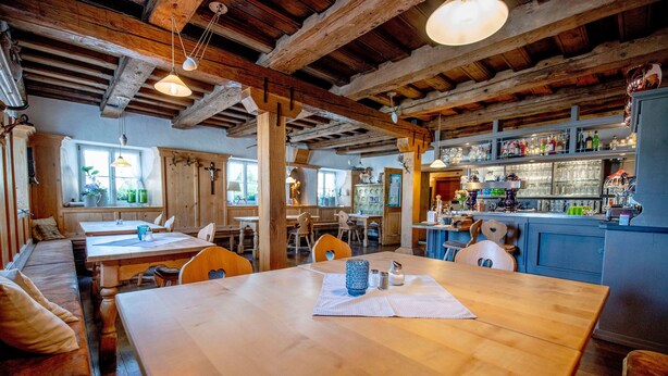 A rustic interior with wooden beams, a bar area with shelves of bottles, and a seating area with tables and chairs. - Landhaus Krone (Steinach)