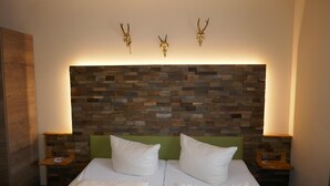 A double bed with white linens, a stone mosaic headboard, and two wall-mounted lamps. - Landhaus Krone (Steinach)