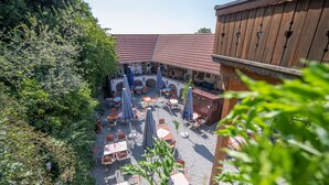 An outdoor courtyard with tables and chairs, surrounded by greenery and a wooden building with a tiled roof. - Landhaus Krone (Steinach)