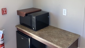 A compact kitchen with a microwave, a small refrigerator, and a built-in oven. - Karbani Inn (Carlsbad)