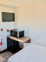 Habitación de hotel compacta con kitchenette, una cama, un televisor de pantalla plana y un detector de incendios.
