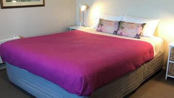 A neatly made bed with a red blanket, a white pillow with a floral design, and a bedside lamp on a nightstand.