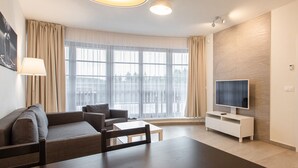 A modern living room with a sofa, a dining table, a TV, and large windows with curtains.