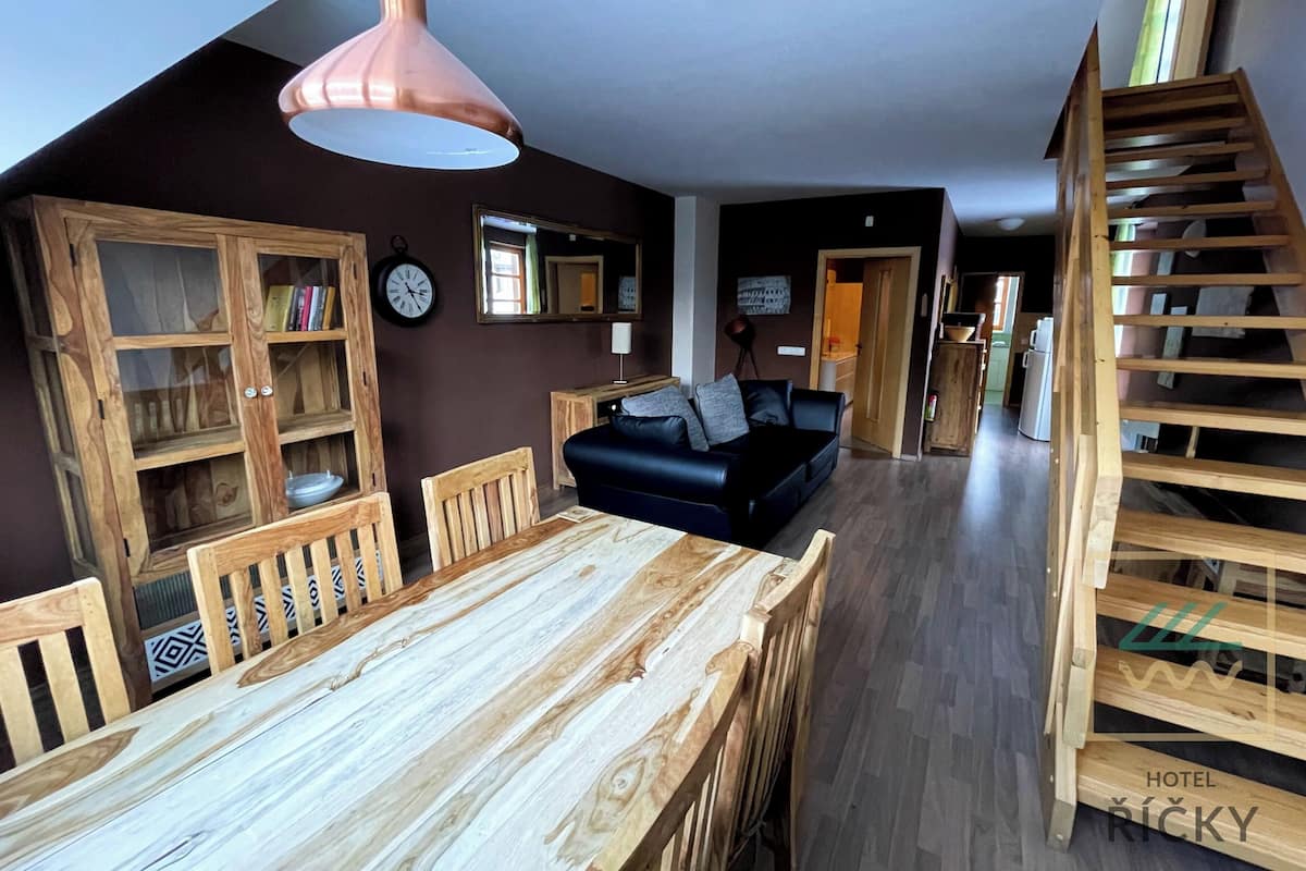 A cozy room with a wooden dining table, a black sofa, and a wooden staircase.