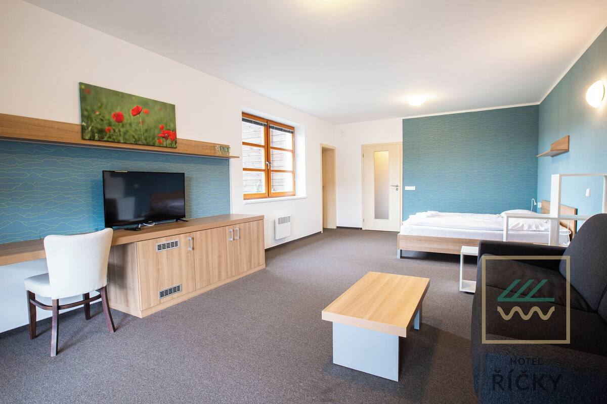 A modern hotel room with a TV, wooden desk, white chair, sofa, and a bed.