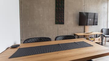 A modern dining area with a wooden table, black chairs, a black woven placemat, a mounted flat-screen TV, and a decorative wall piece.